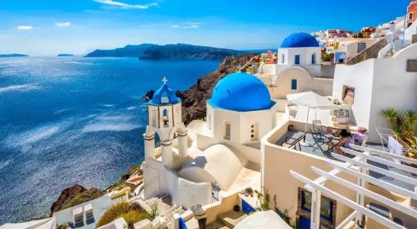 Białe domy z niebieskimi kopułami na greckich wyspach, Santorini, z widokiem na turkusowe morze.