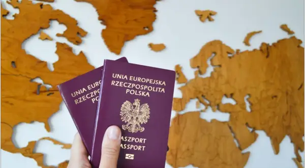 Dwa polskie paszporty, w tym paszport tymczasowy dla dziecka, na tle drewnianej mapy Europy.