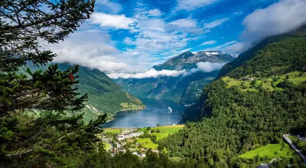 Widok na malownicze fiordy Norwegii, z górami porośniętymi lasem, jeziorem i statkiem wycieczkowym.
