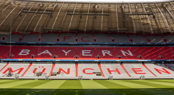 Puste trybuny Allianz Arena z napisem "BAYERN MÜNCHEN" w czerwonych i białych siedzeniach.