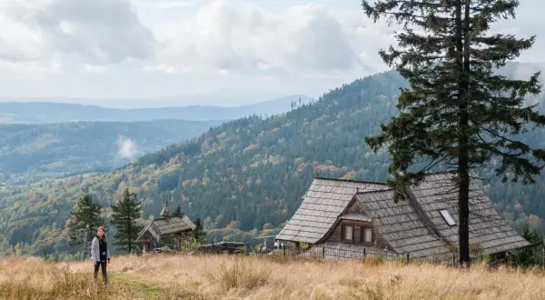 Widok na malownicze góry w Polsce. Drewniany domek i samotna turystka na tle jesiennych lasów i pagórków.