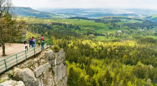 Widok na zielone wzgórza i lasy z platformy widokowej. W oddali widać zabudowania. To piękna kotlina kłodzka.