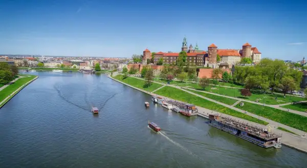 Widok na Wawel i rzekę Wisłę z łodziami. Słoneczny dzień zachęca do spacerów po zielonych bulwarach.