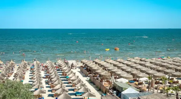 Słoneczny dzień na plaży nad Morzem Czarnym w Rumunii. Rzędy parasoli, ludzie kąpiący się i pływający.