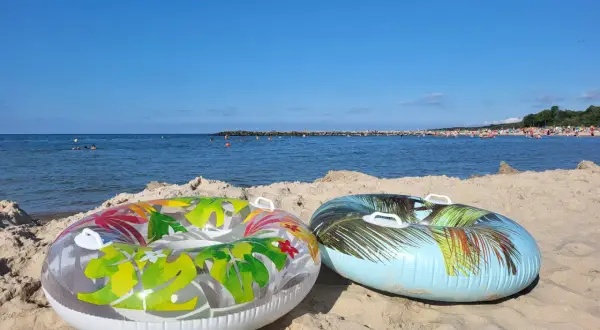 Dwa dmuchane koła na piaszczystej plaży, morze i tłumy ludzi w tle. Idealne na wakacje.pl opinie.