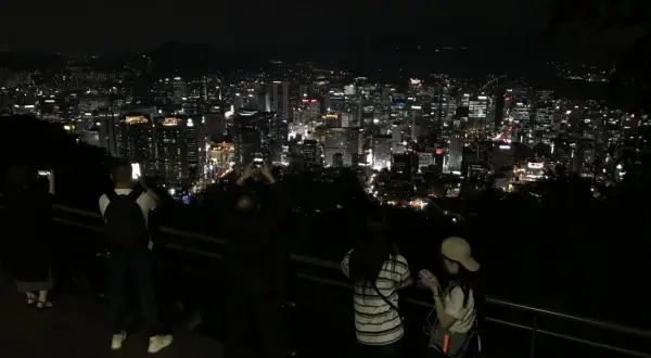 Nocny widok na rozświetlone miasto, przypominające panoramę Gangnam. Ludzie robią zdjęcia, podziwiając miejski krajobraz.