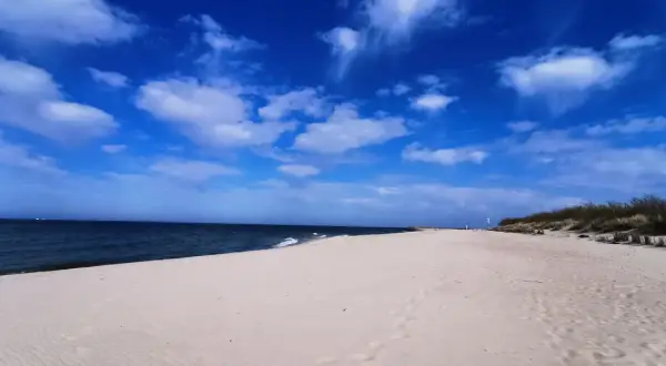 Piękna, słoneczna pogoda na sierpień nad morzem. Szeroka, piaszczysta plaża, spokojne morze i błękitne niebo z białymi chmurami.