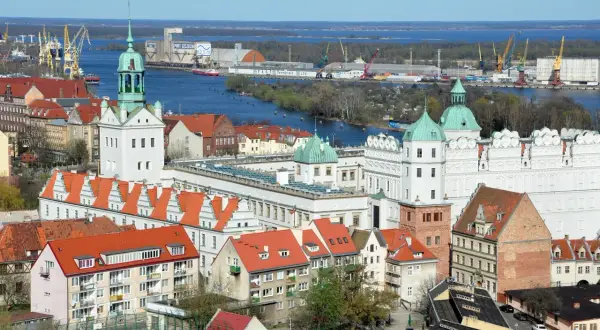 Widok na port w Szczecinie z żurawiami, statkami i zabudowaniami miejskimi.