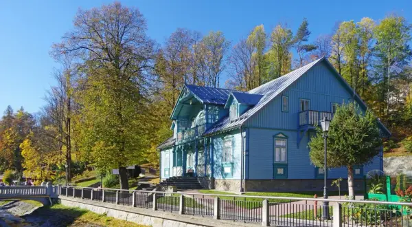 Piękny, błękitny budynek sanatorium Nida-Zdrój otoczony jesiennymi drzewami. Wiele pozytywnych **sanatorium Nida-Zdrój opinie** potwierdza urok tego miejsca.