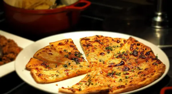 Kawałki pizzy z serem i ziołami na białym talerzu.