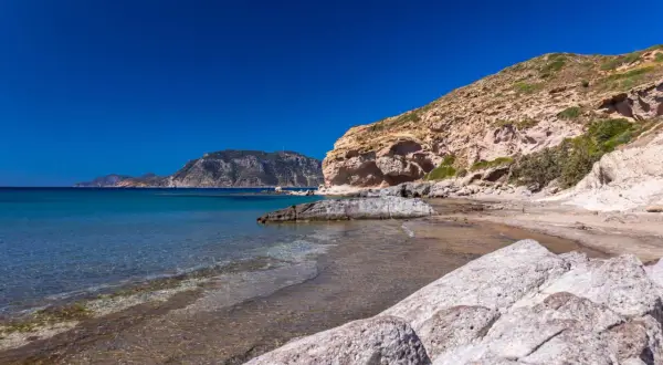 Majowa pogoda na Kos: skalista plaża z turkusową wodą i łagodnymi falami, w tle góry.