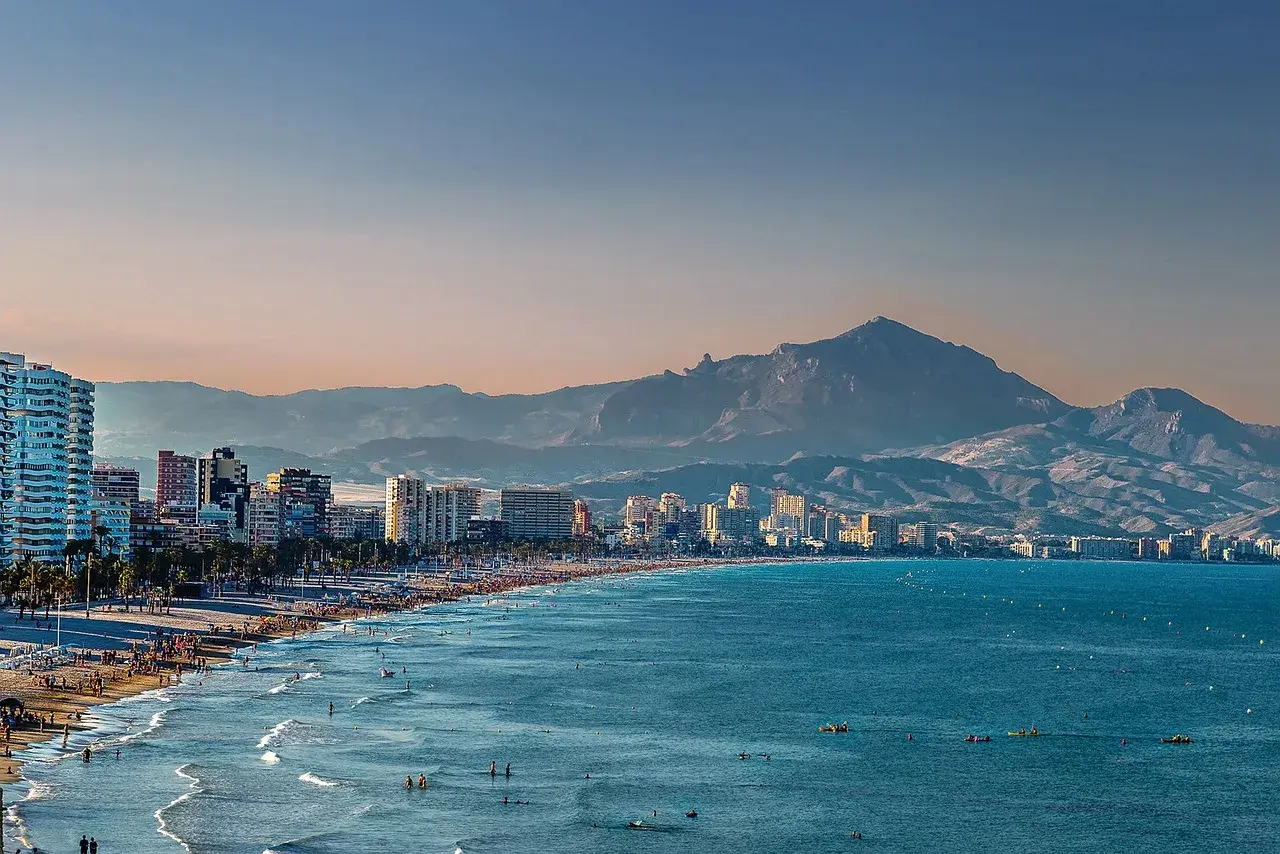 Alicante w grudniu: słoneczna plaża pełna ludzi, turkusowe morze i góry w tle. Idealna pogoda na spacer.