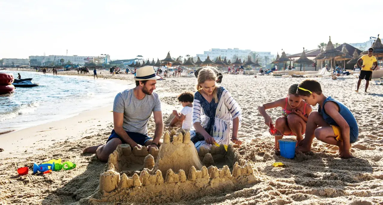 Rodzina buduje zamek z piasku na plaży, idealne miejsce na tunezja wycieczki. Dzieci bawią się z rodzicami, tworząc wspomnienia.