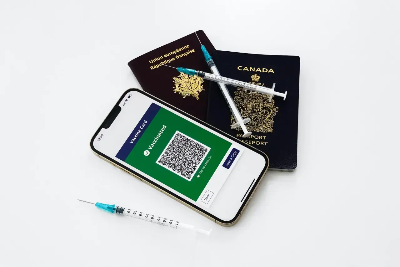 Gotowi na podróż? Paszporty, telefon z potwierdzeniem szczepień i strzykawki symbolizują przygotowania do wyjazdu.