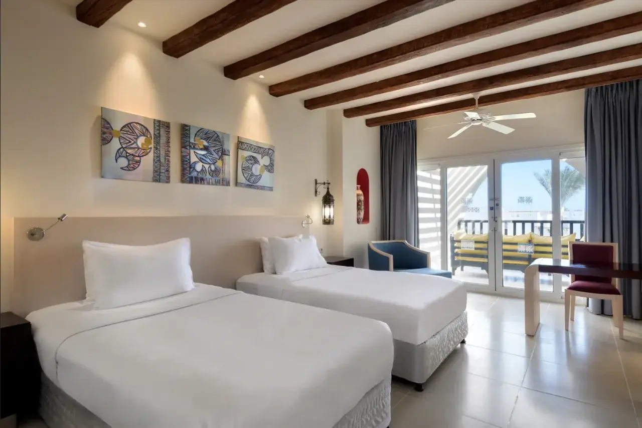 Pokój w Hilton Marsa Alam Nubian Resort. Dwa białe łóżka, obrazy w stylu nubijskim, balkon z widokiem na morze.