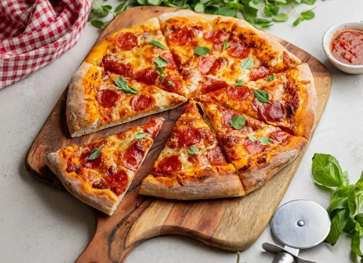 Pyszna pizza pepperoni z ciągnącym serem i świeżą bazylią, pokrojona na kawałki, czeka na desce.