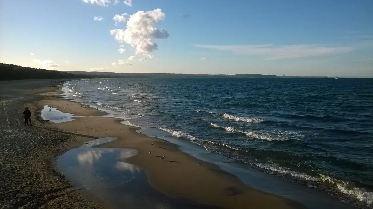 Spokojna plaża Jelitkowo o zachodzie słońca. Woda faluje, a na piasku widać kałuże i mewy.