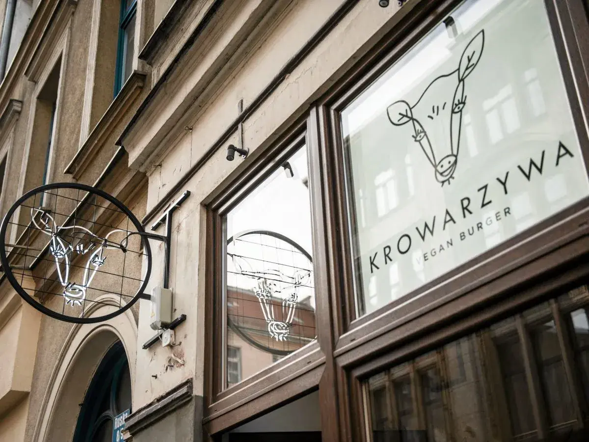 Neonowy znak i logo na szybie lokalu Krowarzywa. Wesoła krowa zaprasza na wegańskie burgery.