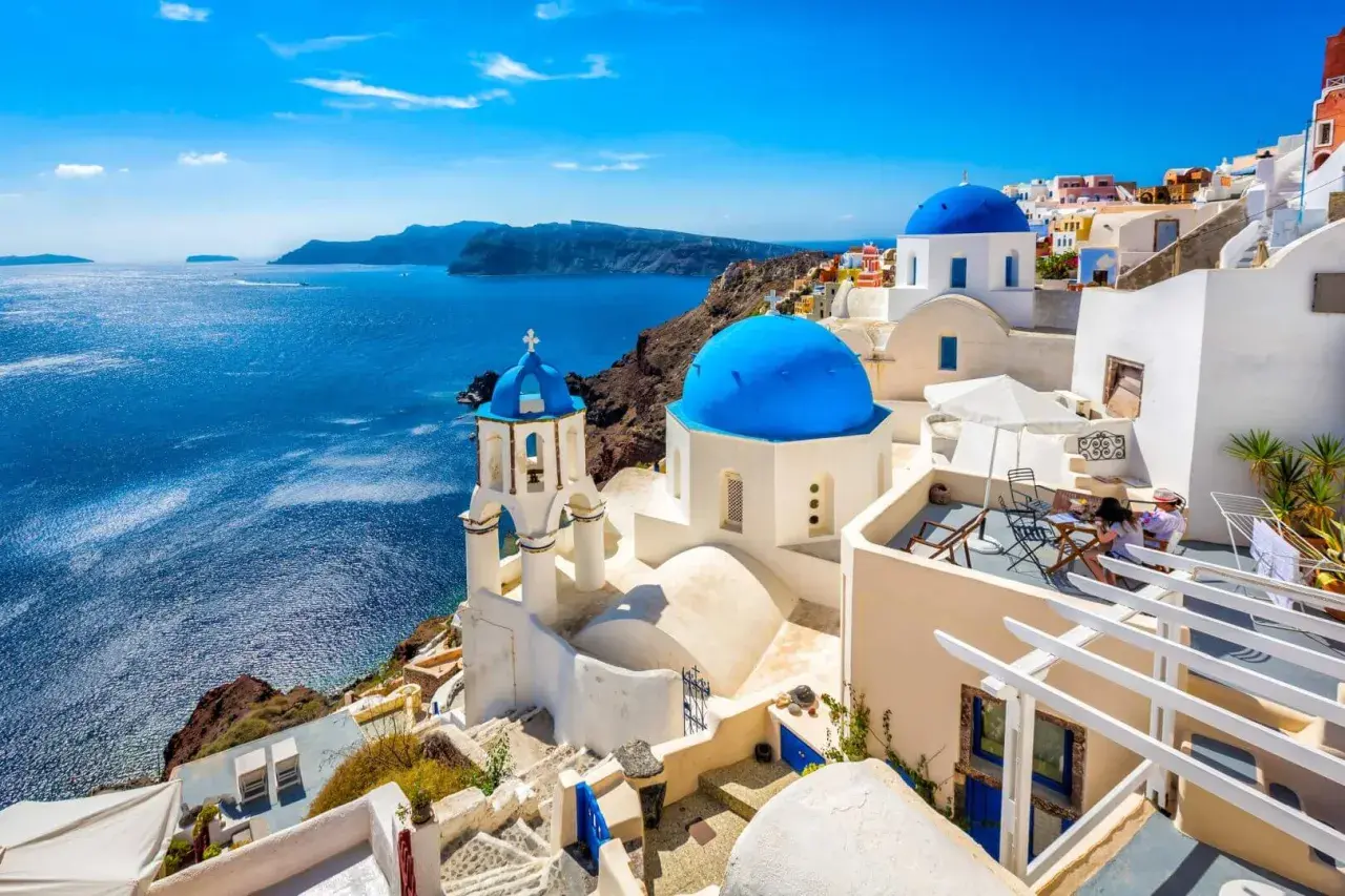 Białe domy z niebieskimi kopułami na greckich wyspach, Santorini, z widokiem na turkusowe morze.