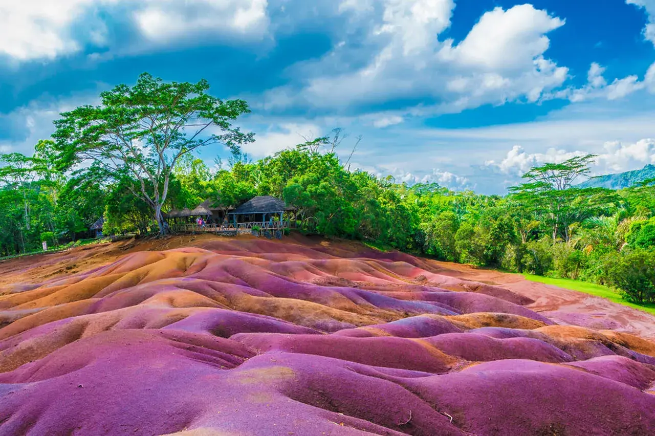 Kolorowe wydmy na Mauritiusie, które warto zobaczyć. W tle bujna zieleń i chmury.