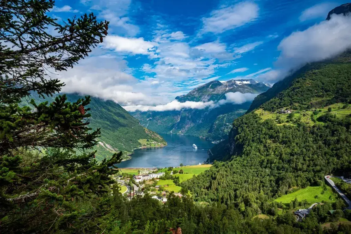 Widok na malownicze fiordy Norwegii, z górami porośniętymi lasem, jeziorem i statkiem wycieczkowym.