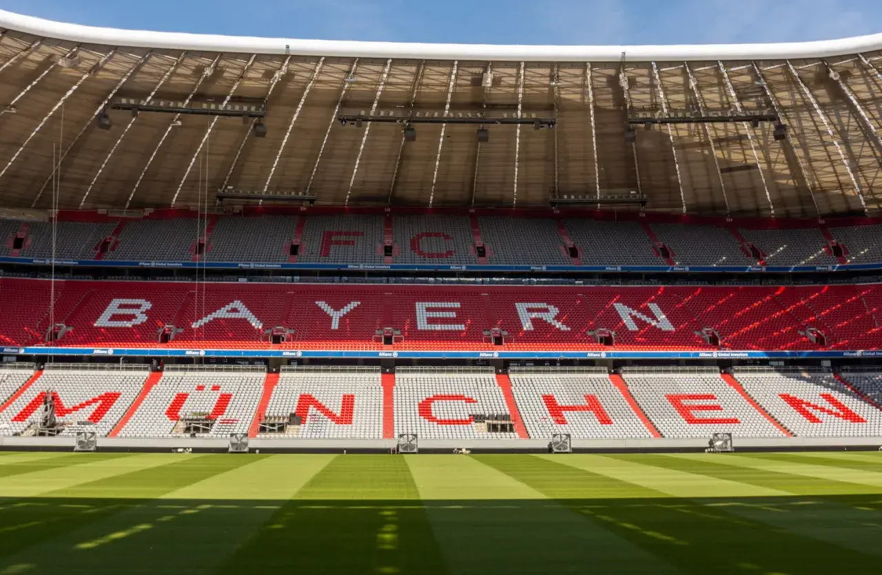 Puste trybuny Allianz Arena z napisem "BAYERN MÜNCHEN" w czerwonych i białych siedzeniach.