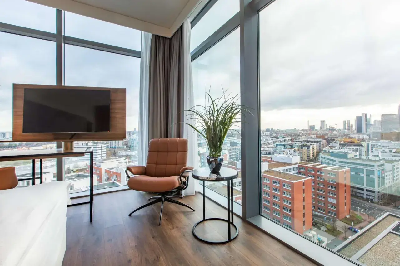 Wygodny fotel i telewizor w pokoju hotelowym z widokiem na panoramę Frankfurtu. Frankfurt Radisson Blu oferuje wspaniałe widoki.