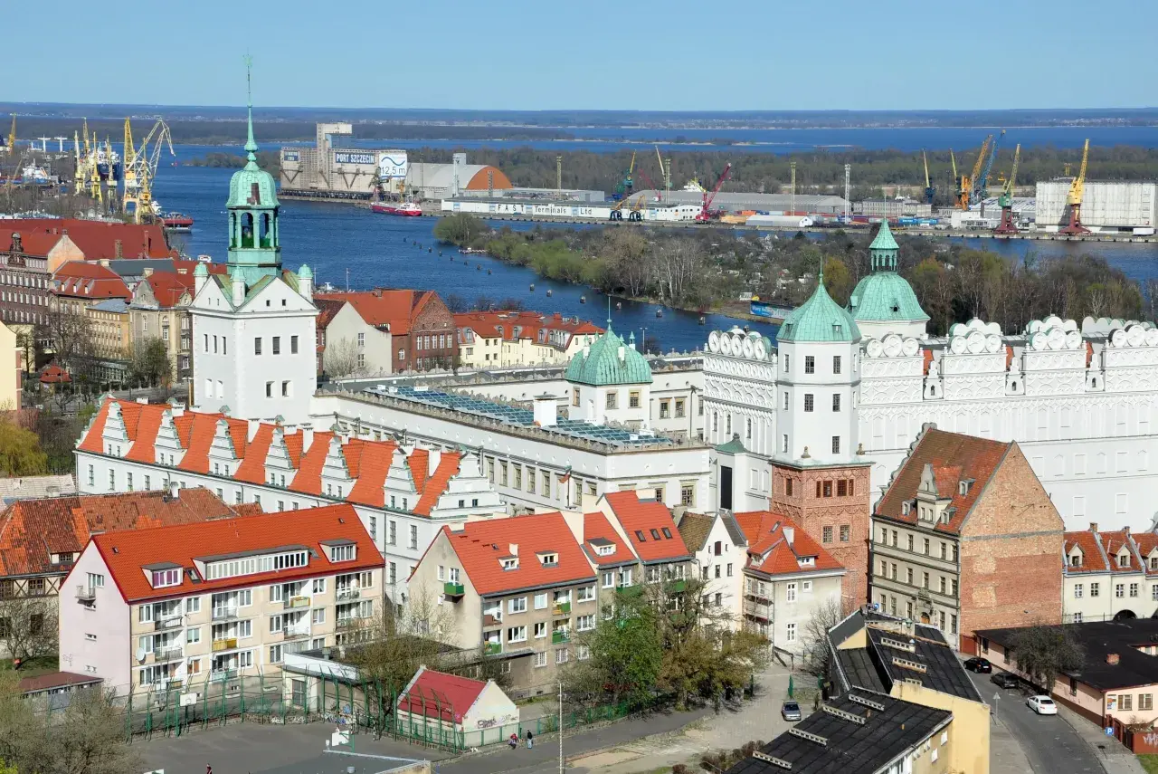 Widok na port w Szczecinie z żurawiami, statkami i zabudowaniami miejskimi.