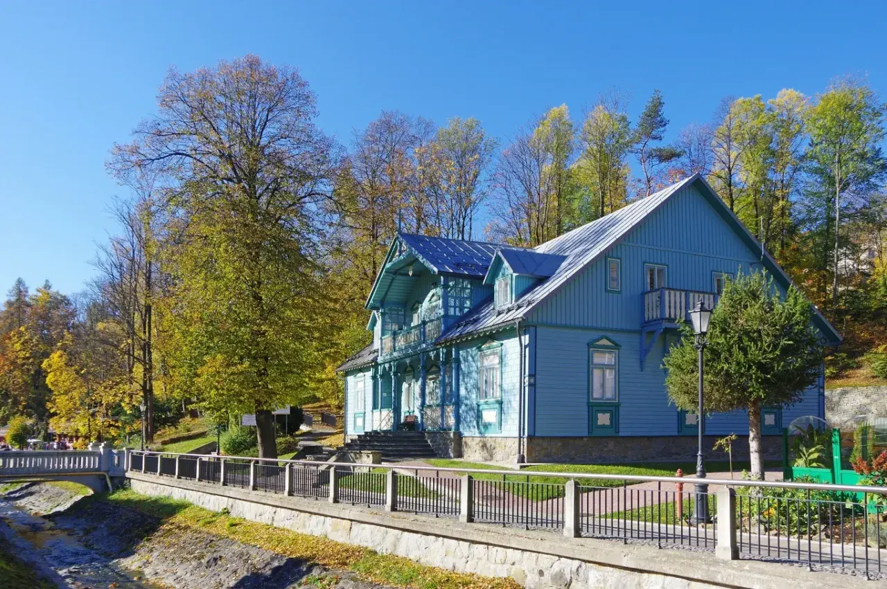 Piękny, błękitny budynek sanatorium Nida-Zdrój otoczony jesiennymi drzewami. Wiele pozytywnych **sanatorium Nida-Zdrój opinie** potwierdza urok tego miejsca.
