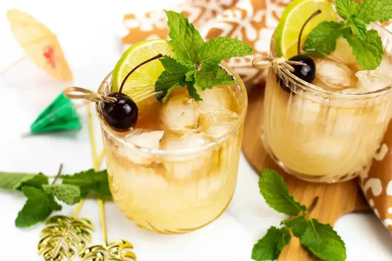 Dwa orzeźwiające drinki Mai Tai z lodem, limonką, wiśnią i miętą, ozdobione parasolkami.