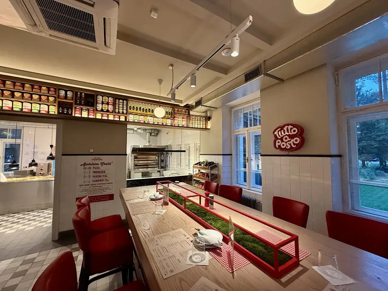 Wnętrze restauracji z długim stołem, czerwonymi krzesłami i piecem do pizzy. Otto Pompieri opinie pozytywne, warto odwiedzić!