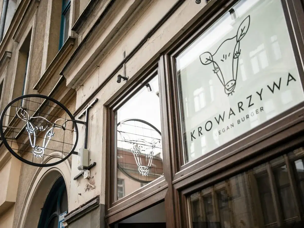 Neonowy znak i logo na szybie lokalu Krowarzywa. Wesoła krowa zaprasza na wegańskie burgery.
