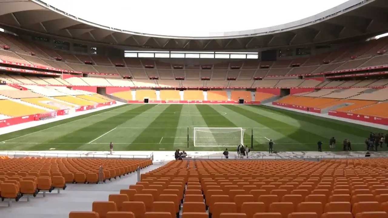 Pusta trybuna stadionu La Cartuja z pomarańczowymi siedzeniami i zieloną murawą.