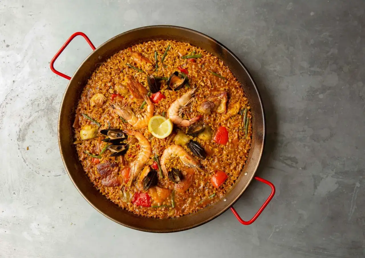 Pyszne hiszpańskie jedzenie: paella z owocami morza, krewetkami, małżami i warzywami, udekorowana cytryną.