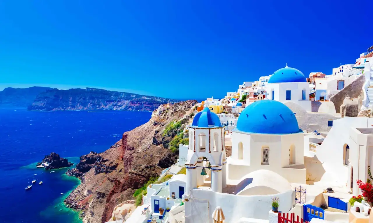 Santorini, idealne miejsce, gdzie na wakacje w sierpniu. Białe domy z niebieskimi kopułami na tle lazurowego morza i klifów.