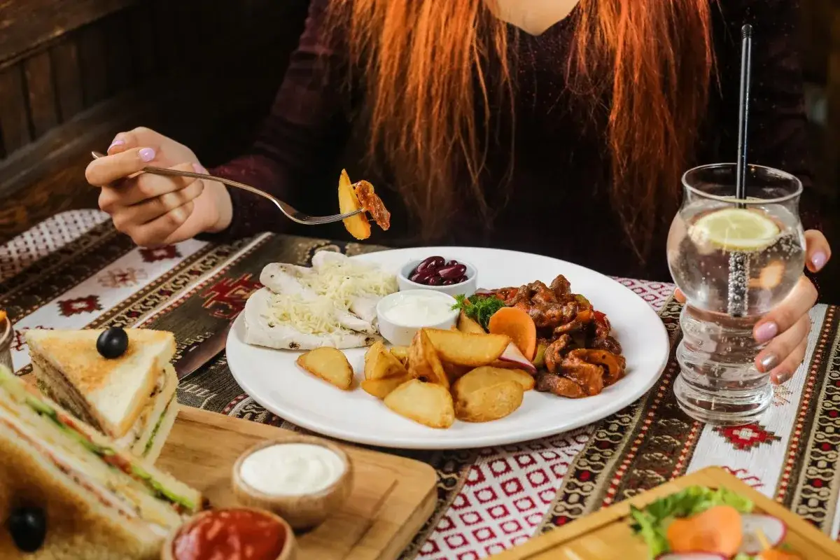 Smaczny posiłek w Michałowej Gospodzie. Widok na talerz z mięsem, frytkami, plackami i fasolką. W tle drink z cytryną.