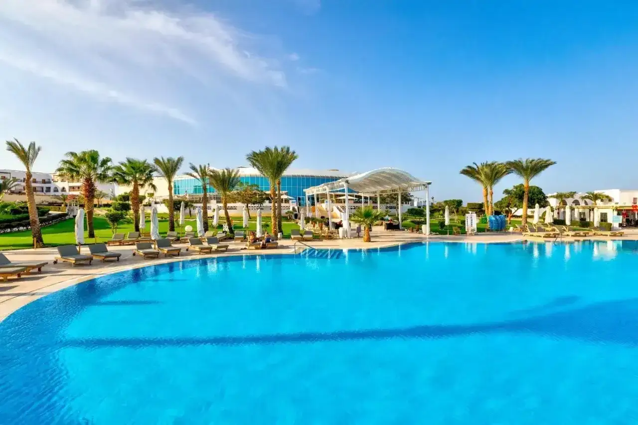 Basen z turkusową wodą i leżakami, palmy, zielony trawnik i budynki hotelowe. Wiele pozytywnych hilton marsa alam nubian resort opinie potwierdza ten widok.