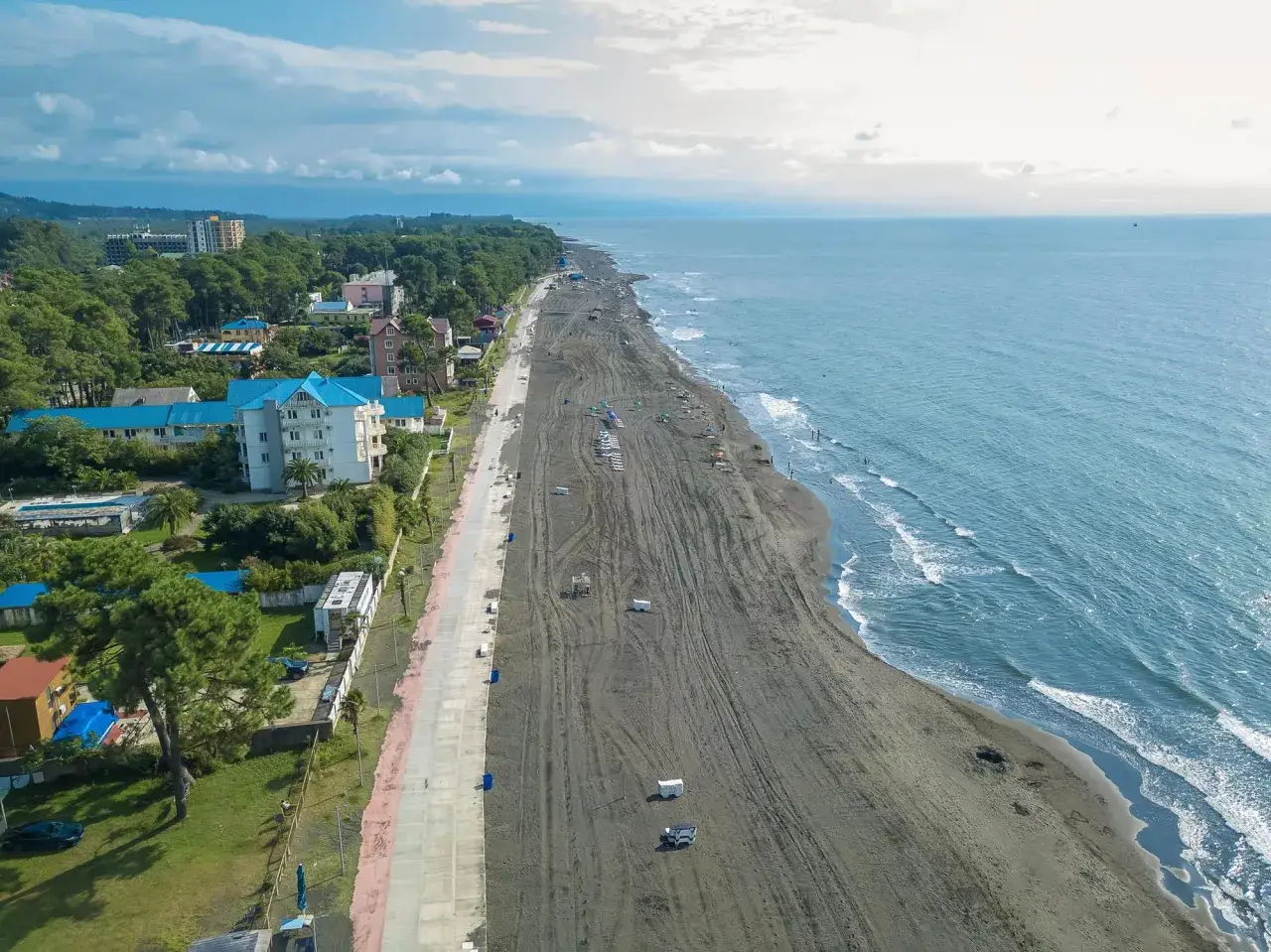 Szeroka, piaszczysta plaża nad Morzem Czarnym w Gruzji, z hotelami i zielenią w tle.