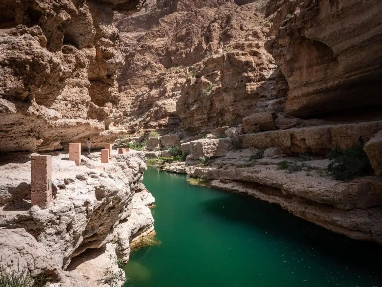 Wadi Shab w państwie Oman. Zielona woda w kanionie, skalne ściany i pojedynczy turysta.