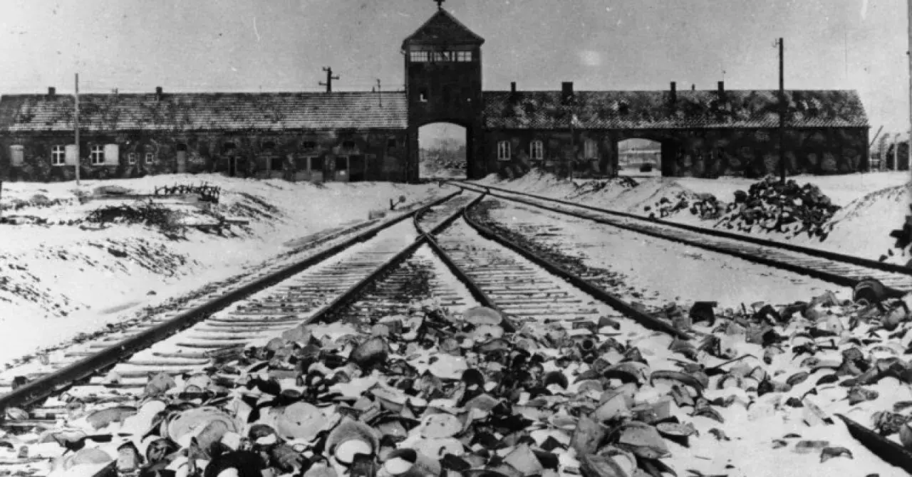 Brama obozowa Auschwitz-Birkenau w zimowej scenerii. Kolejowe tory prowadzą do bramy, a przed nimi leżą stosy przedmiotów. Państwowe Muzeum Auschwitz-Birkenau w Oświęcimiu opinie świadczą o jego ważności.