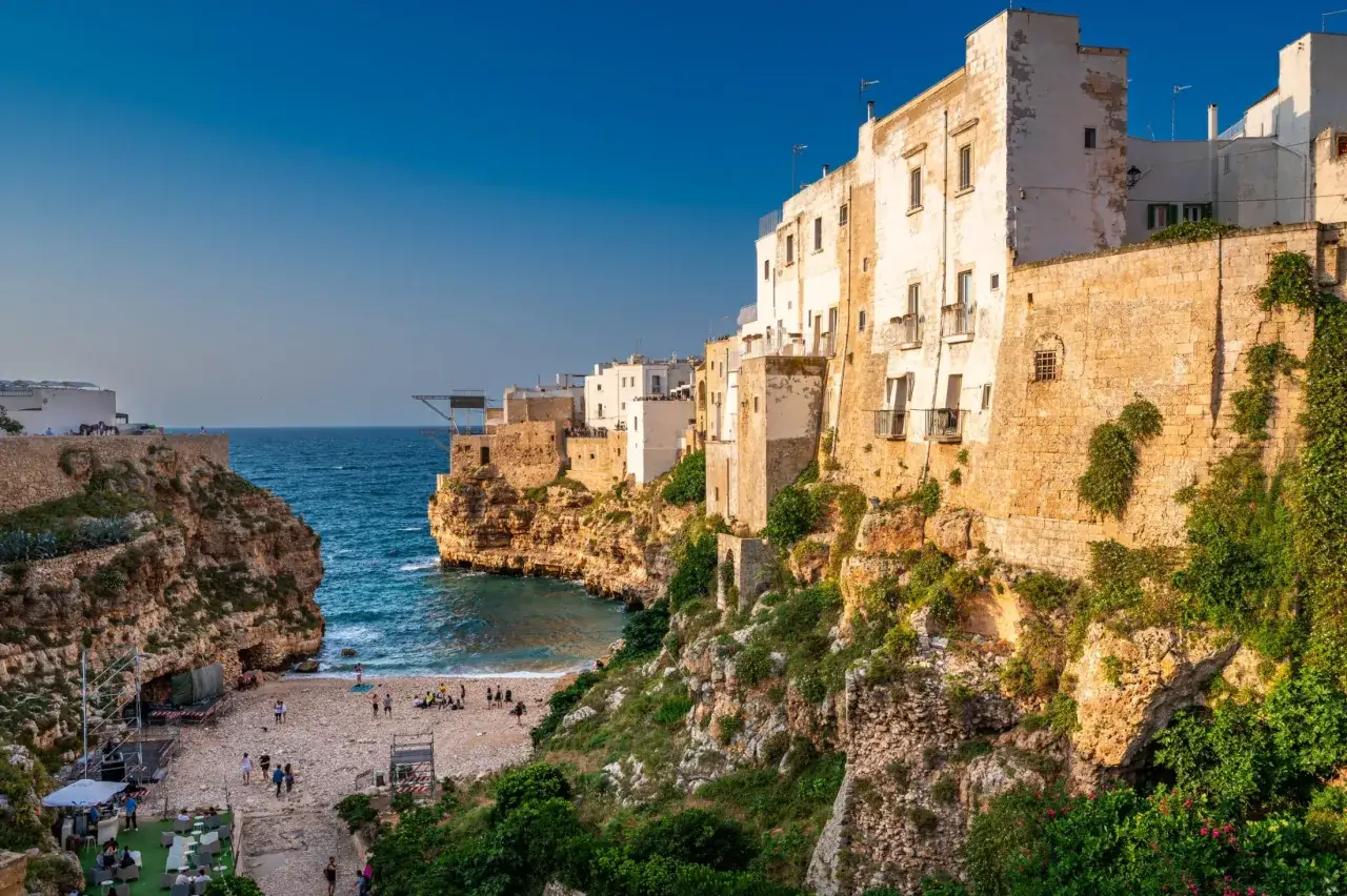 Polignano a Mare, Apulia. Wspaniała pogoda w październiku nad Adriatykiem. Białe domy na klifie, plaża z ludźmi i turkusowa woda.