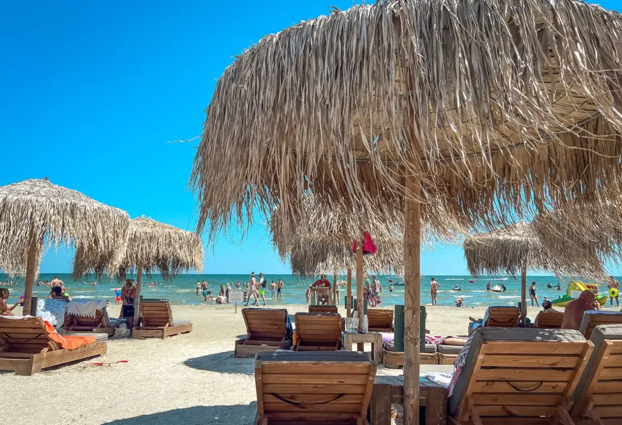Słoneczny dzień na plaży w Rumunii nad Morzem Czarnym. Leżaki i parasole z trawy zapraszają do odpoczynku.