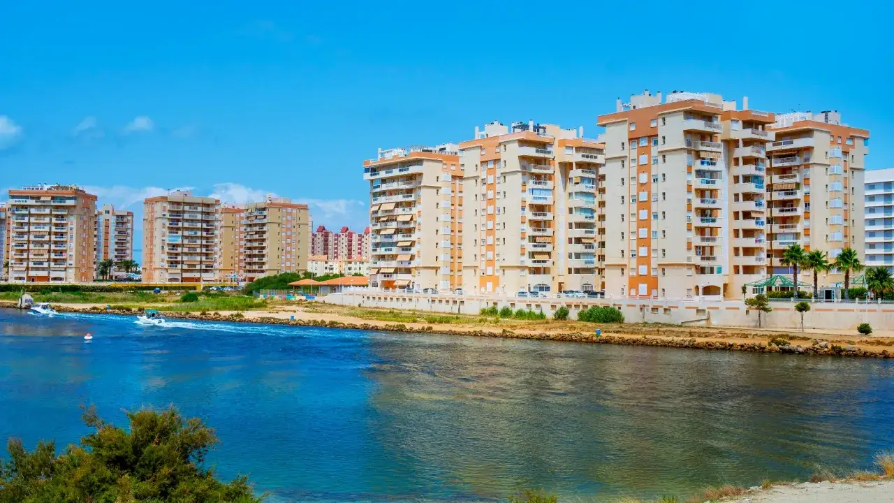 Nowoczesne apartamentowce nad wodą w La Manga, Hiszpania. Dwie łodzie płyną po błękitnej wodzie.