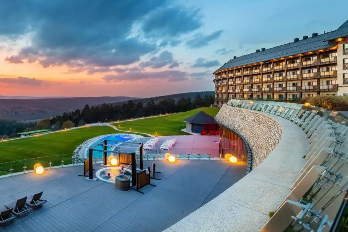 Luksusowy Kempinski Hotel z basenem i jacuzzi na tarasie, otoczony zielonymi wzgórzami o zachodzie słońca.