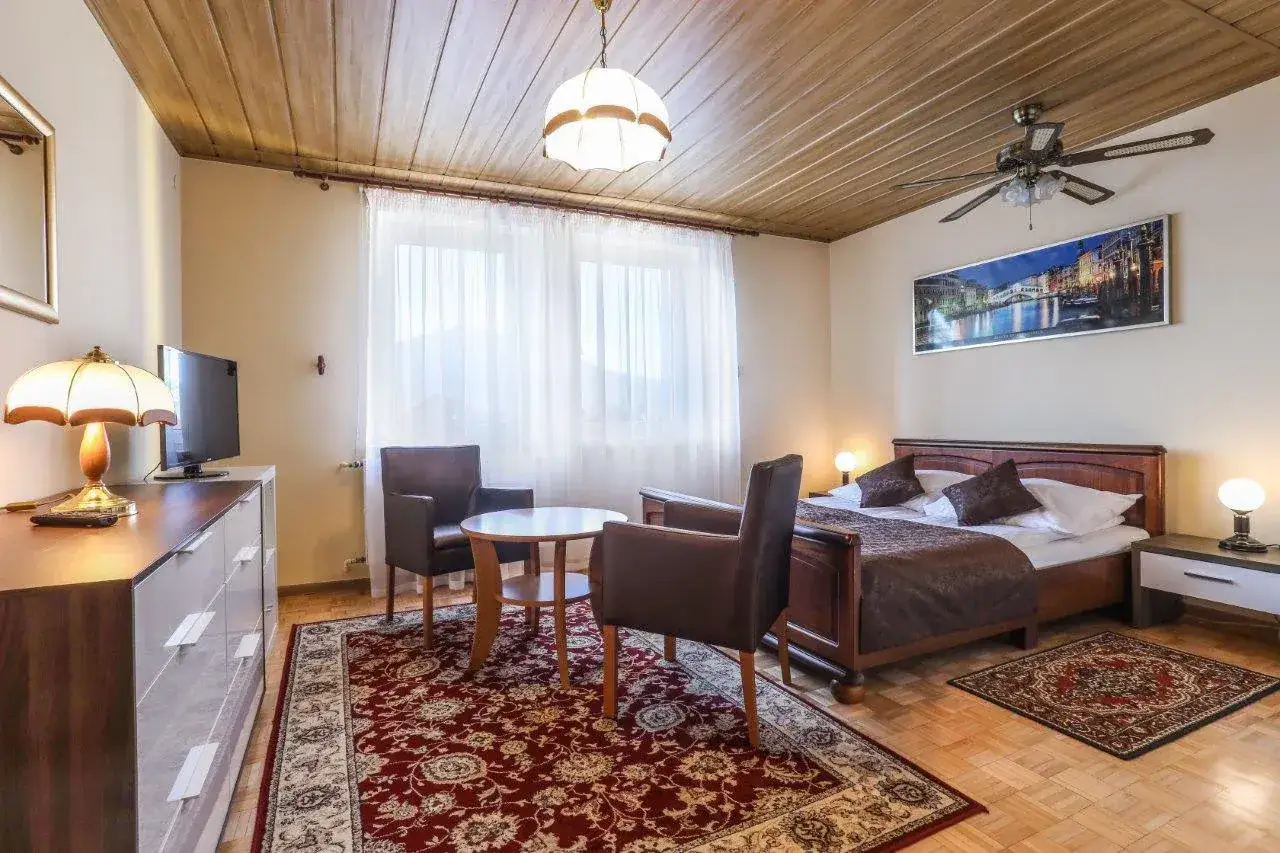 Przytulny pokój w hotelu Milena Milówka. Łóżko, fotele, stolik i komoda tworzą komfortową przestrzeń.