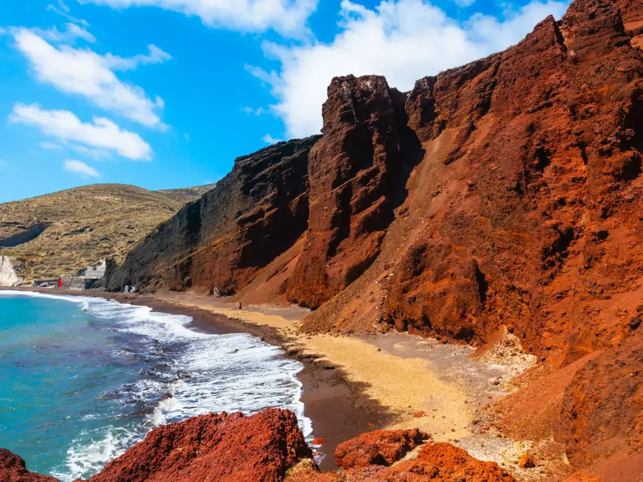 Niezwykłe santorini plaże z czerwonymi klifami i turkusową wodą. Piasek plaży ma odcień pomarańczowy, a skały są w kolorze rdzy.