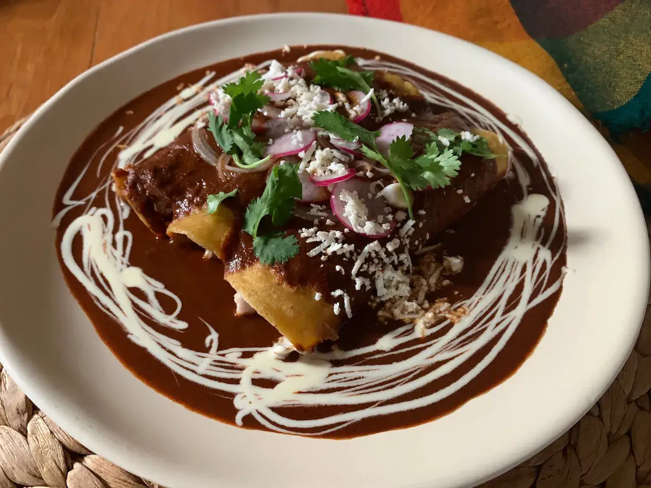 Pyszne dania meksykańskie: enchiladas w sosie mole, posypane serem, rzodkiewką i kolendrą, polane śmietaną.