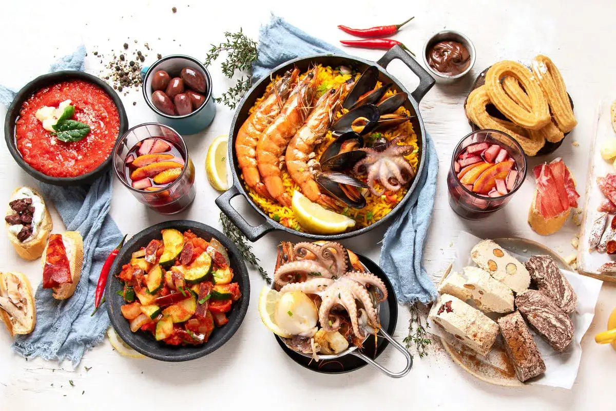 Pyszne tapas i paella, czyli prawdziwa kuchnia hiszpańska. Na stole owoce morza, oliwki, churros i sangria.
