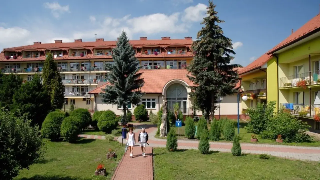 Sanatorium Nida-Zdrój: pozytywne opinie pacjentów potwierdzają urokliwy ogród i profesjonalną opiekę. Dwie osoby spacerują po ścieżce.