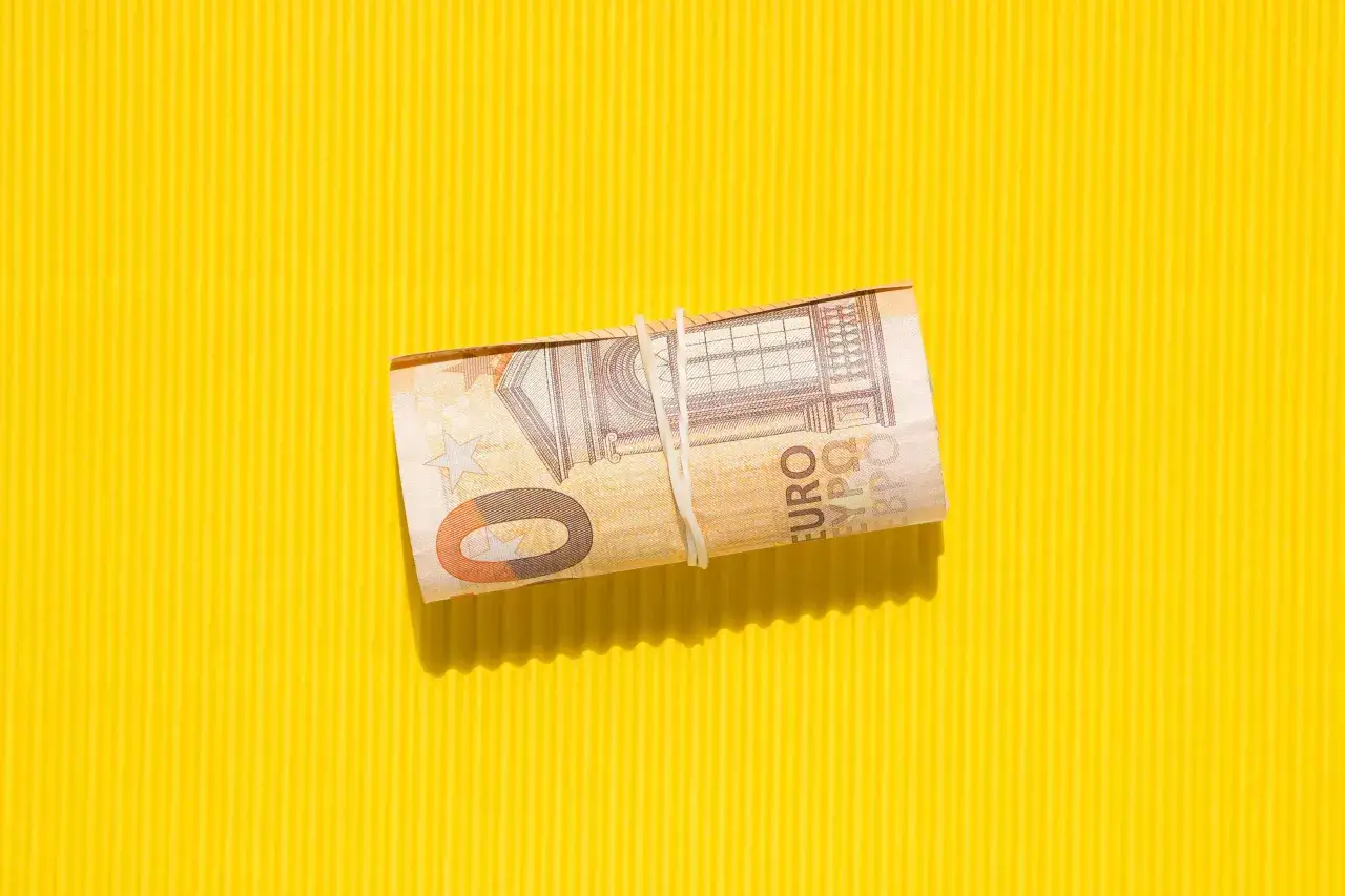 Zrolowane banknoty euro, które kiedyś były walutą Łotwy, leżą na żółtym tle.
